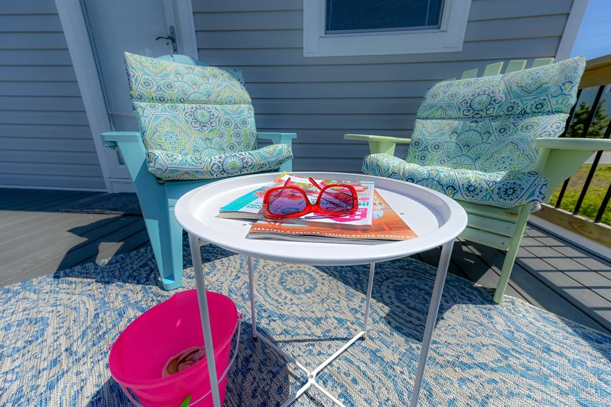 A vibrant outdoor scene with colorful chairs, a table holding magazines and sunglasses, and a decorative rug, set up in a way that invites reading, relaxation, and conversation in the fresh air.