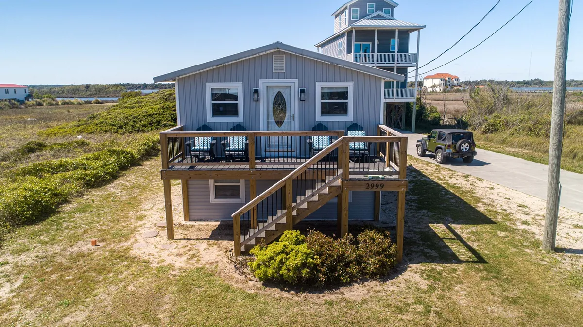 This photo captures a spacious wooden deck at the front of the home, featuring inviting outdoor seating, a decorative glass front door, and ample space for gathering. The scene is peaceful, ideal for morning coffee or relaxing at sunrise, with soft light suggesting an early start to the day.