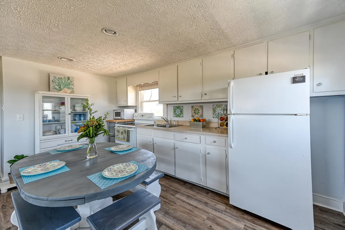 A cheerful kitchen and dining space with a dining table, flower vase, kitchen cabinets, and refrigerator. The setup encourages shared meals, cooking, and spending time together—activities typical of a flexible, affordable vacation base.