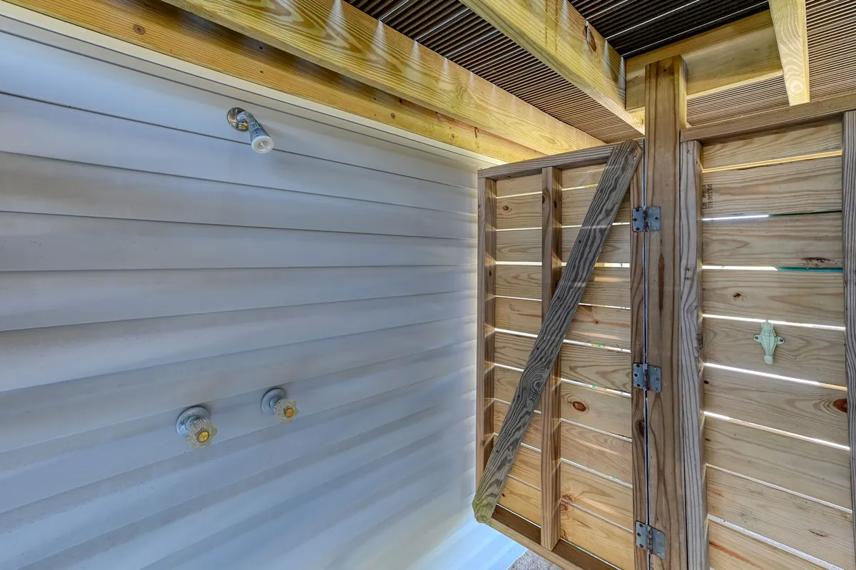 A fresh, inviting outdoor shower framed by a wooden door and textured walls. Natural sunlight brightens the space, evoking the feeling of rinsing off after a day on the water.