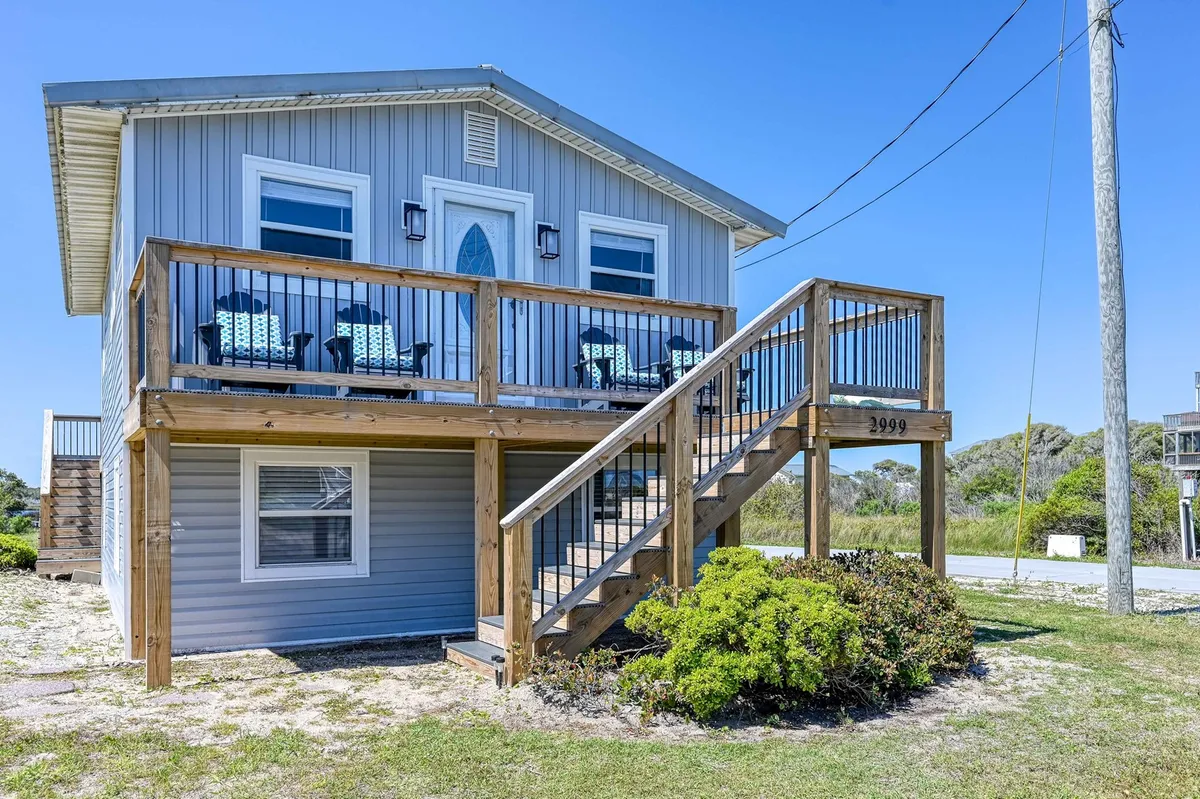 A welcoming wooden deck with blue chairs and a staircase leading down, positioned to take in the coastal views. The space is perfect for gathering, relaxing, and watching sunsets with the family.