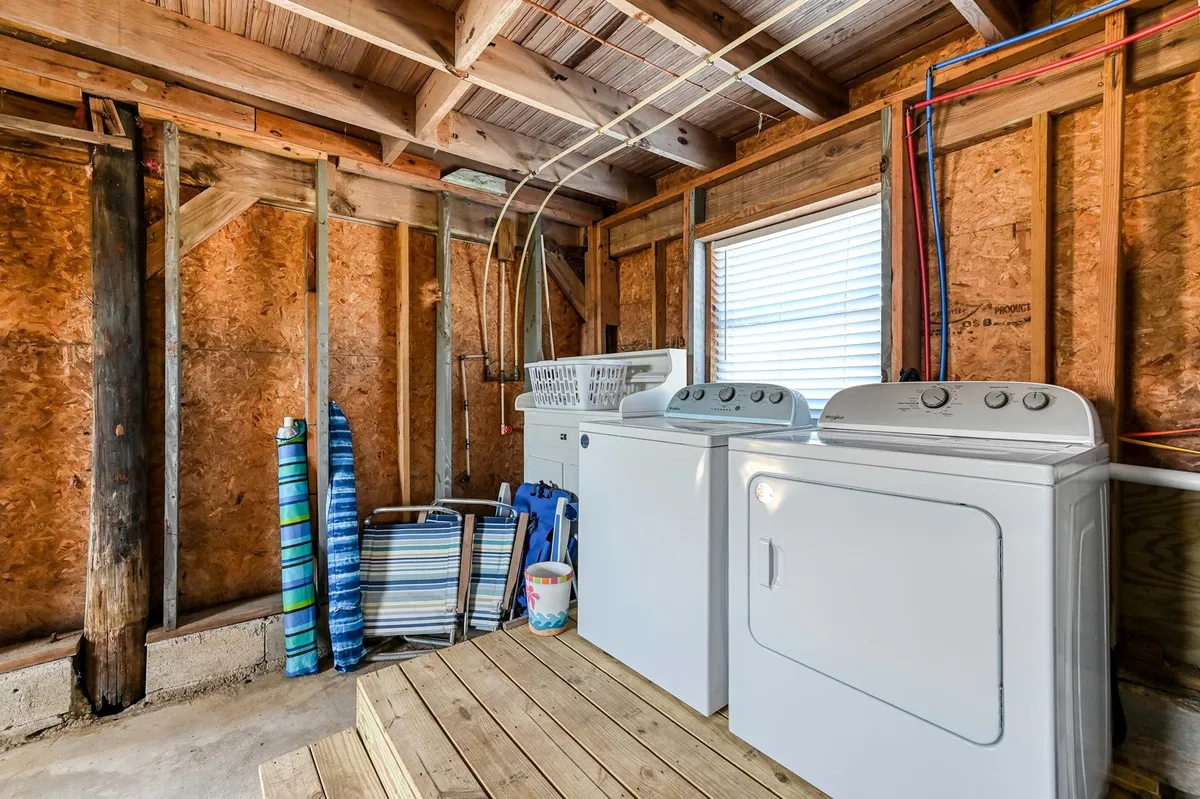 A compact, functional laundry area with a washing machine, dryer, laundry basket, and folding chairs. The space feels orderly and practical, ideal for tackling family chores after a day outdoors.