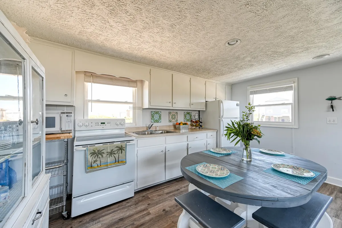 A cheerful dining area adjacent to an open kitchen, featuring a classic wooden dining table, decorative plates, modern kitchen appliances, and a window that offers lovely views outside. The setup exudes a timeless, welcoming vibe, ideal for family meals and lingering conversations.