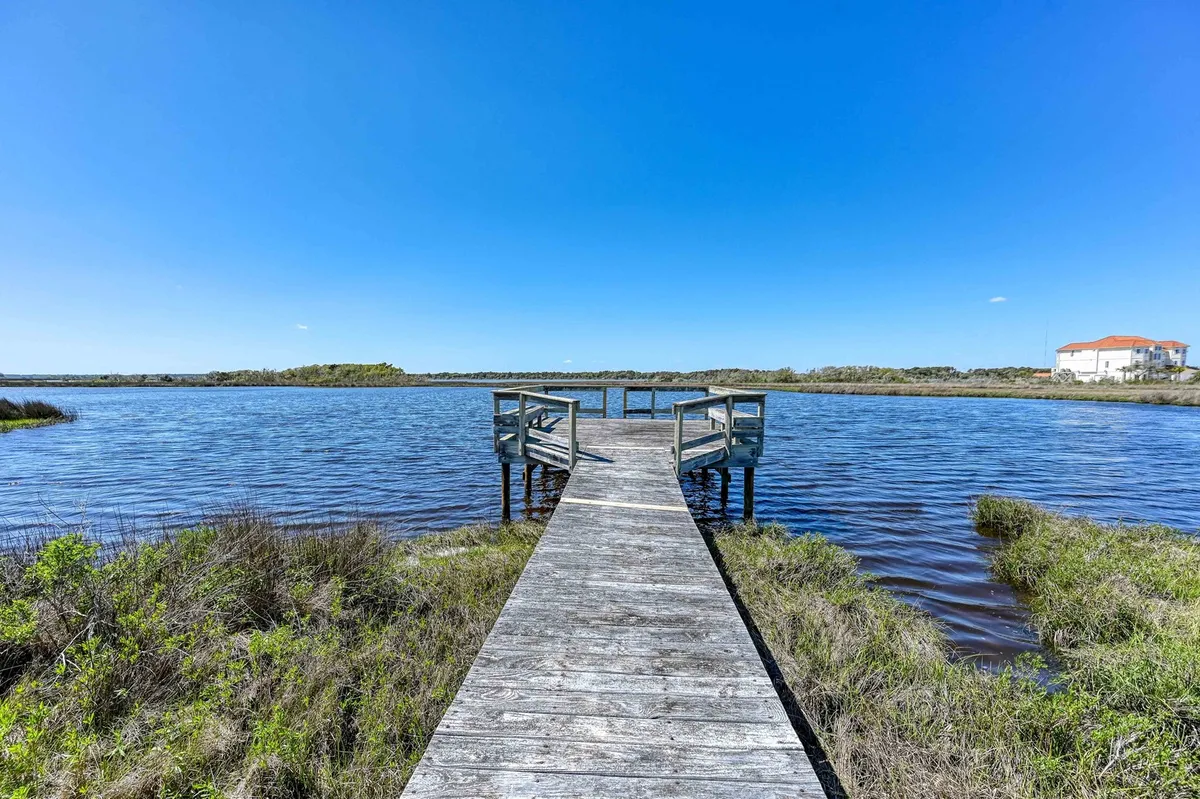 This serene scene highlights a wooden dock extending over calm water, framed by lush greenery. The tranquil mood is perfect for sunset photography, quiet evenings, or simply watching the light reflect across the sound—capturing the peaceful escape promised by the rear deck's view.