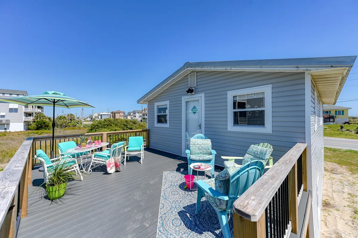 Brightly colored outdoor seating, an umbrella, and a decorative rug create an inviting spot on a deck overlooking open spaces. The setup suggests a place to unwind, enjoy waterfront views, or share a casual meal outdoors.