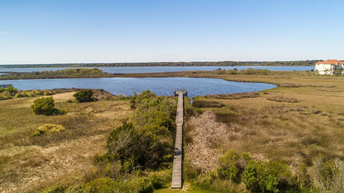 A peaceful wooden dock extends into calm water, surrounded by lush greenery. The setting is tranquil, with opportunities to spot wildlife such as birds or even dolphins, and ideal for launching kayaks or fishing. The image embodies a private, nature-filled waterfront experience.
